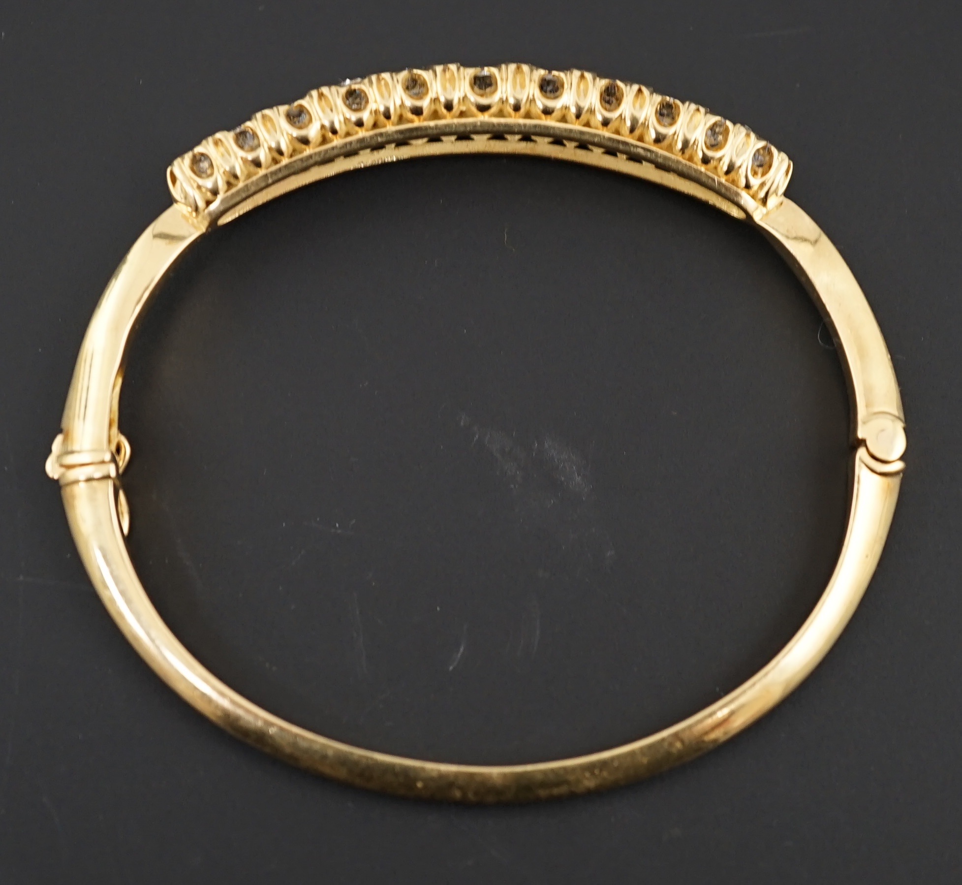 A gold and graduated eleven stone diamond set hinged bangle
